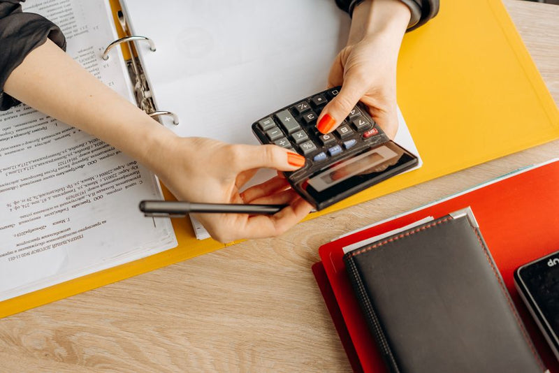 Hands using a calculator over a binder of financial documents