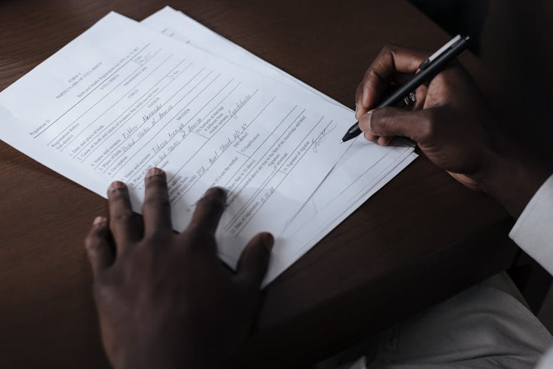 Person filling out and signing an official paper form at a desk