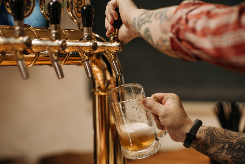 bartender pouring a glass of draft beer behind a wooden bar