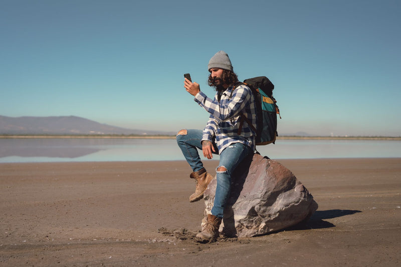 young traveler looking at phone standing beside a parked van on an empty road