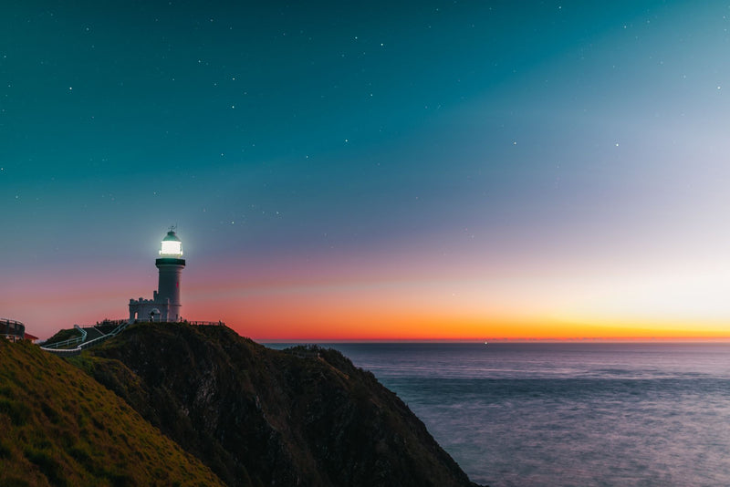 white lighthouse on a green headland above the ocean at sunrise