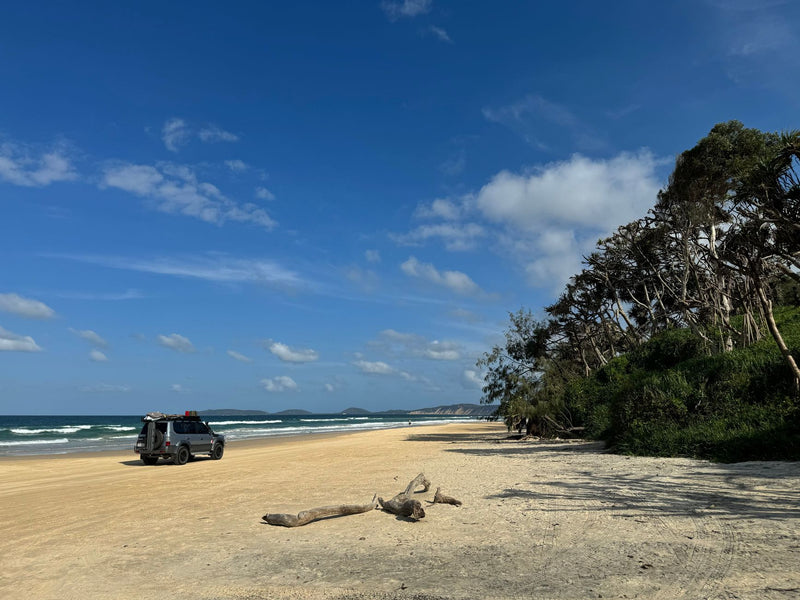 four wheel drive vehicle driving on a wide sandy beach beside forest