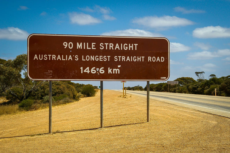 yellow warning road sign on a long empty highway through dry outback
