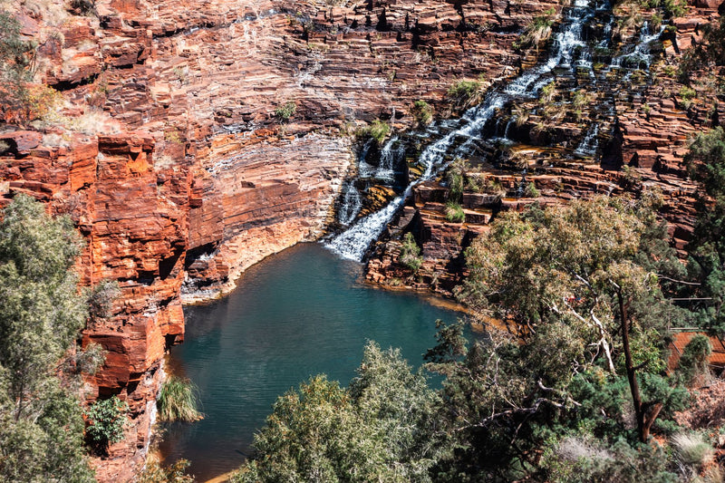 deep red rock gorge with a small waterfall and green pool below