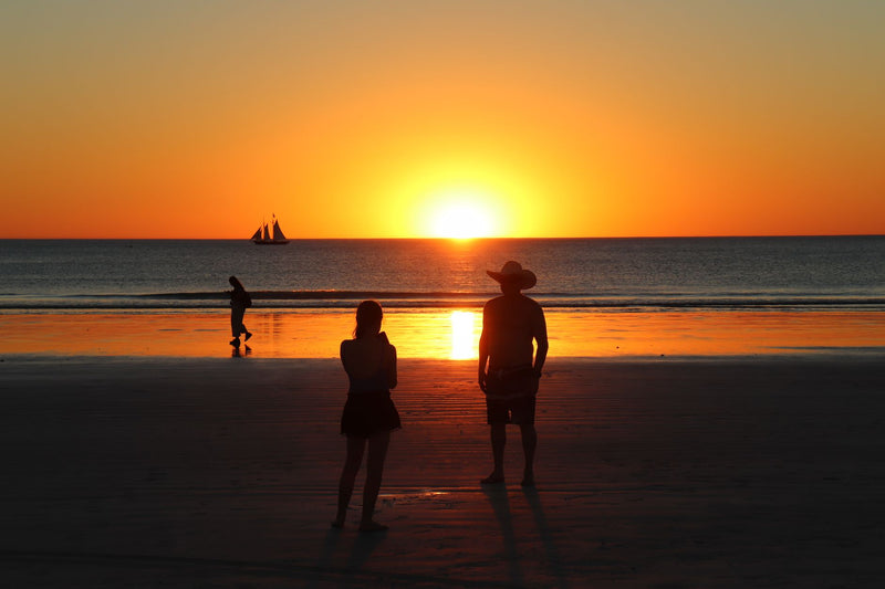 line of camels walking along a wide sandy beach at sunset