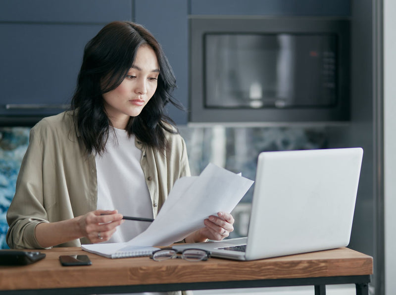 young person reviewing paper documents next to open laptop at wooden table