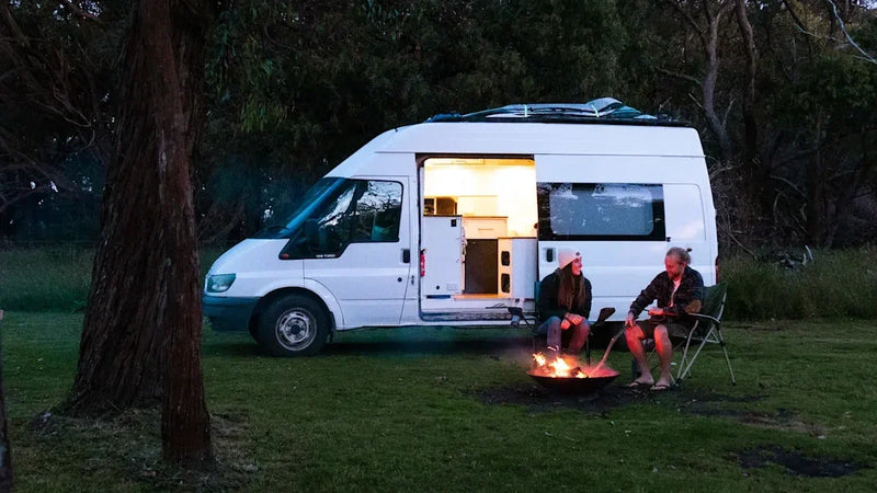 young couple standing beside white camper van reading a map on rural road
