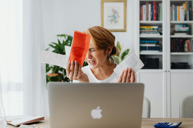 Frustrated woman holding paper receipts at a laptop
